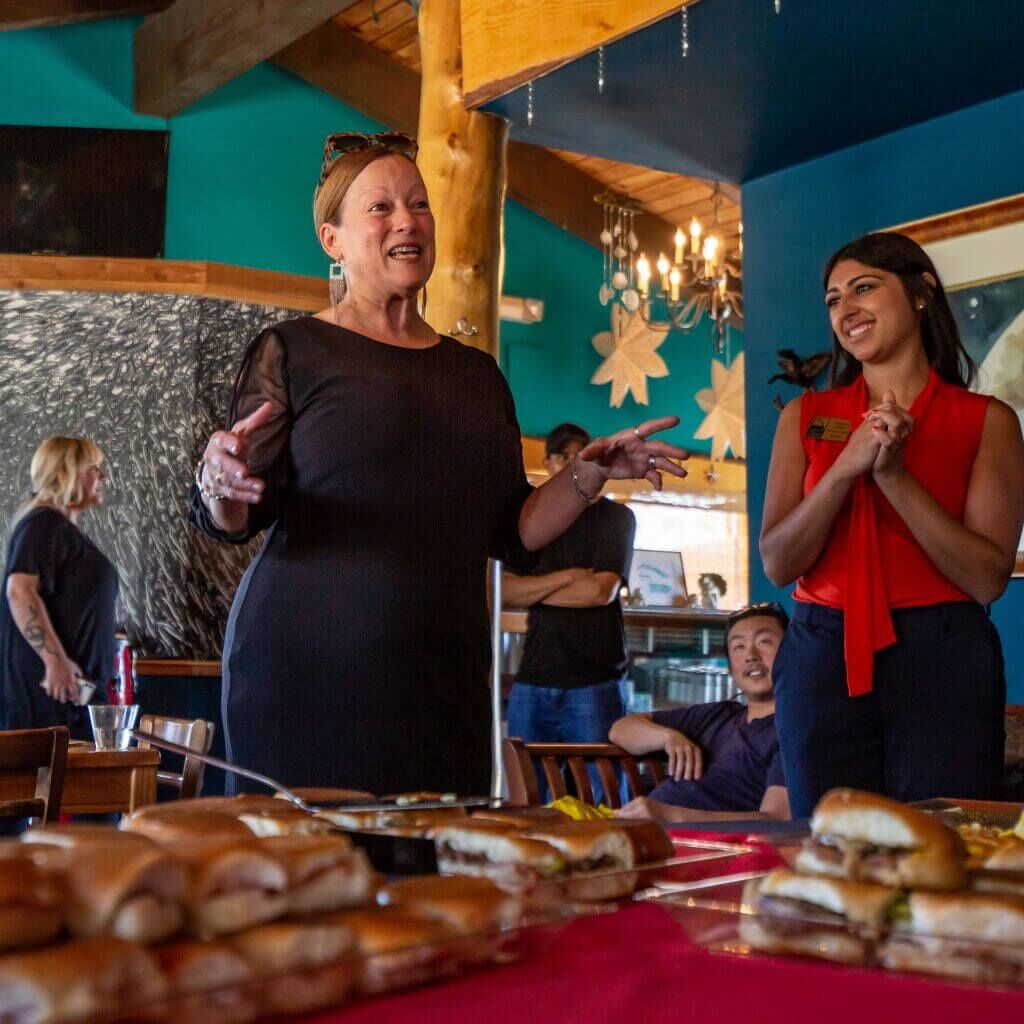 Cristi Quesada-Costa, owner of Dos Alas Cubarican Cafe and Lounge, speaks to Chamber members at her restaurant while Chamber staff Brianna stands next to her smiling